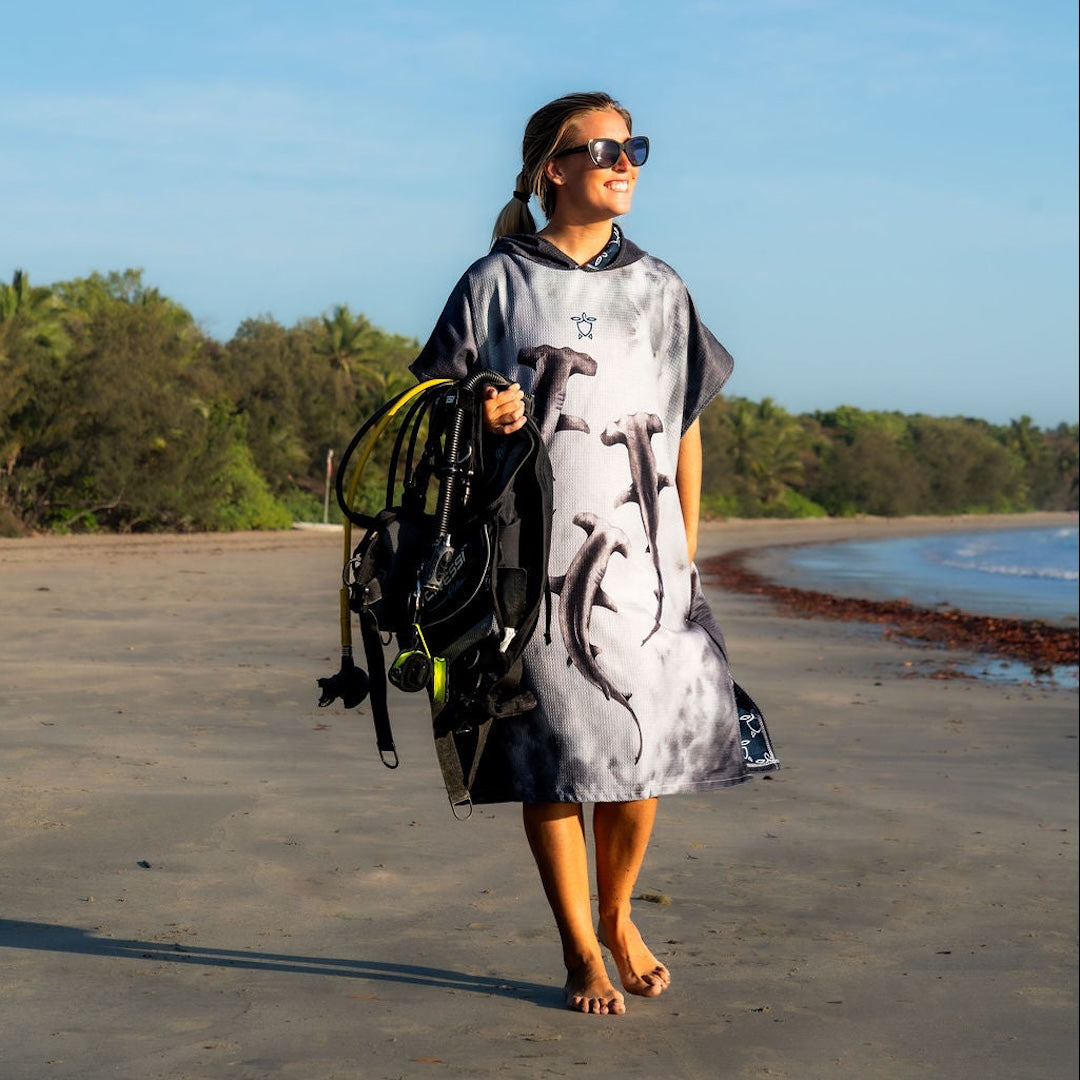 Person on a beach wearing hammerhead changing poncho and carrying dive gear