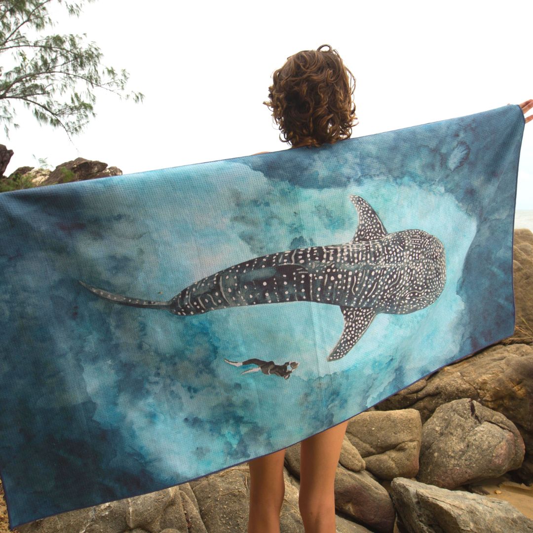 woman  standing on a beach, wrapped in matching light blue hooded towels featuring large sea turtle and whale shark prints.