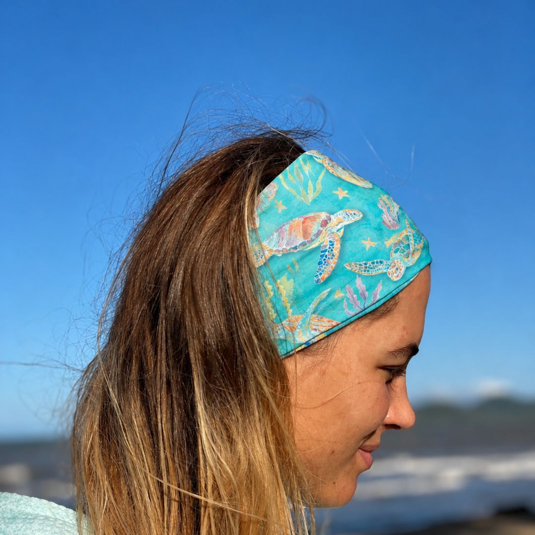 Person wearing a turquoise headband with sea turtle design against a blue sky.
