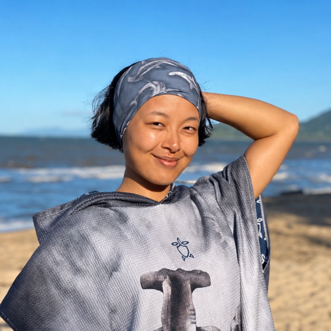 Woman on a beach wearing a sun-buff with a design, smiling at the camera.