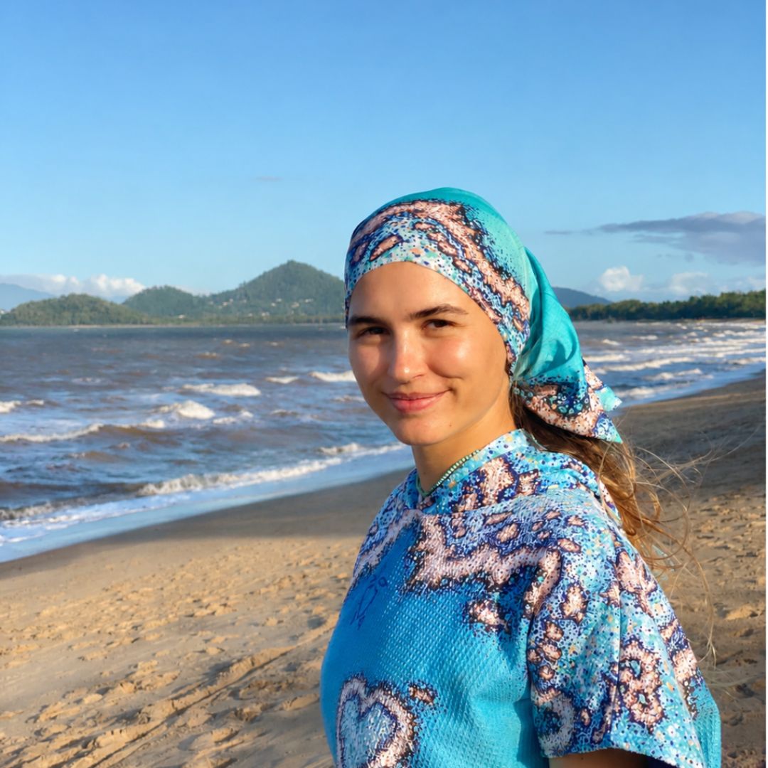 Person at the beach wearing a Reef Love Multi-Use Sun Buff styled as a head wrap with a blue coral reef pattern.