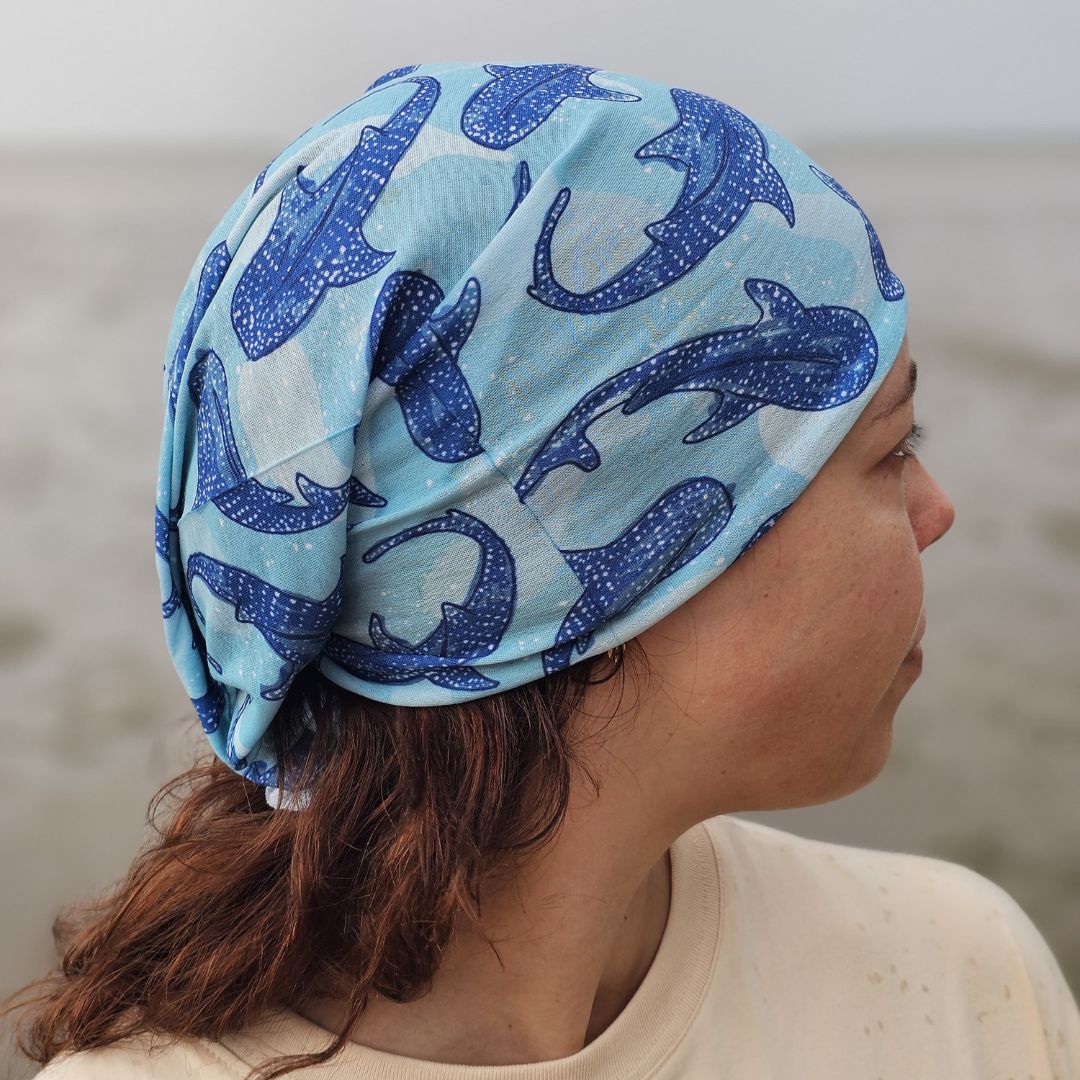 A woman shown in profile wearing a light blue headscarf with a blue whale print, photographed outdoors against a soft-focus gray background.